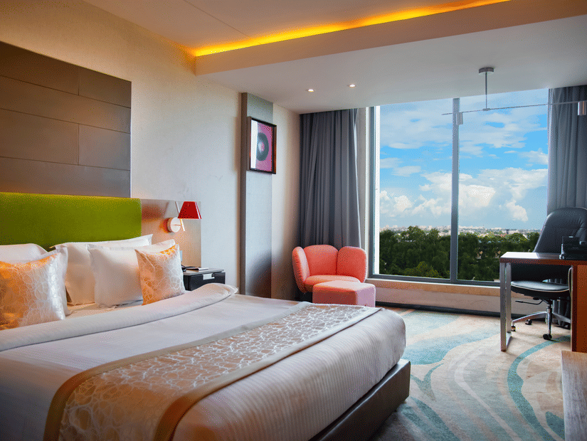 Bedroom at The Regnant featuring double size bed, a sofa,  a work desk and chair, and a large window with view.