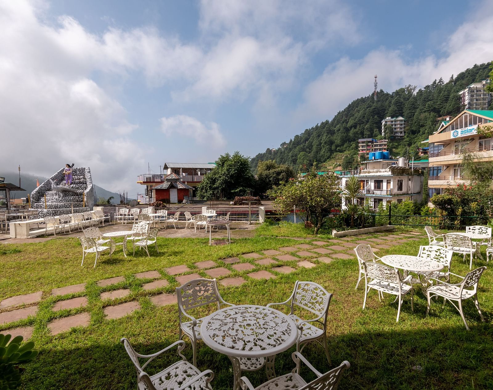 Outdoor seating area with tables and chairs on a lawn overlooking a mountain view - DLS Meghavan Resort