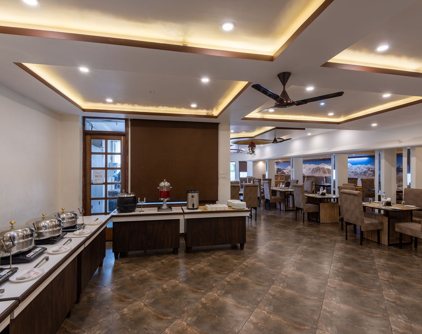 A dining room with tables and chairs, a buffet line, and a ceiling fan - DLS Meghavan Resort