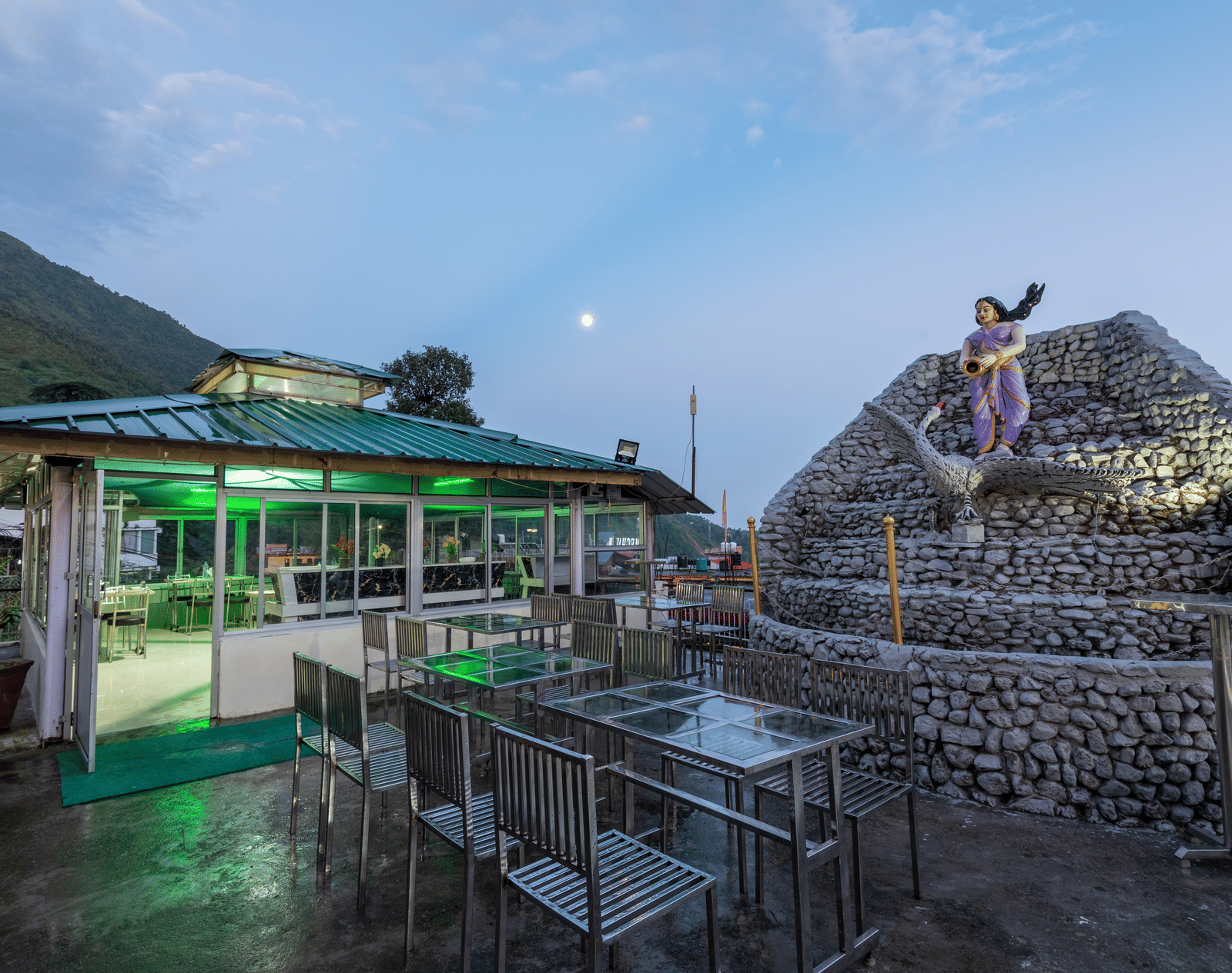 A view of an outdoor dining area at a resort with a stone fountain and a statue in the foreground -  DLS Meghavan Resort
