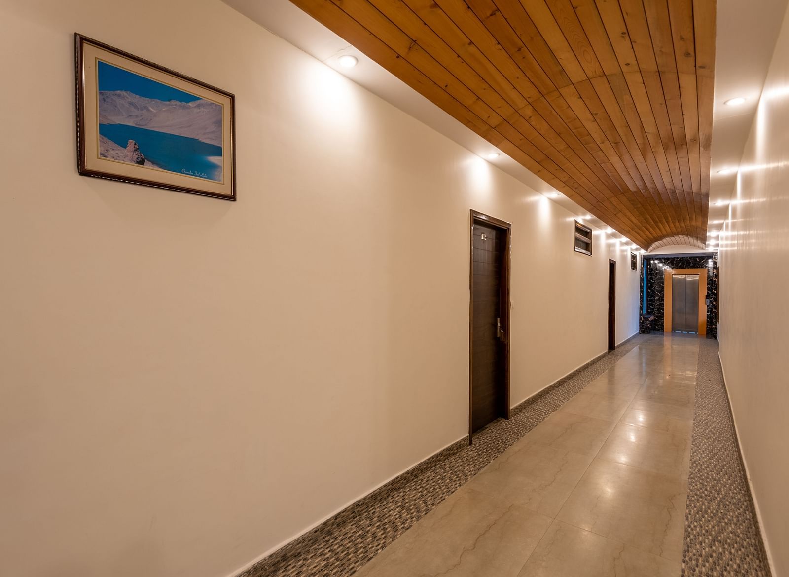 A well-lit hotel hallway with carpeted flooring and guest room doors - DLS Meghavan Resort