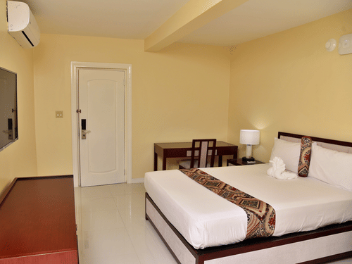 Standard Room at Hotel Grand A View featuring a plush bed facing the TV mounted on the wall over a running table and a work desk with a chair placed by the door