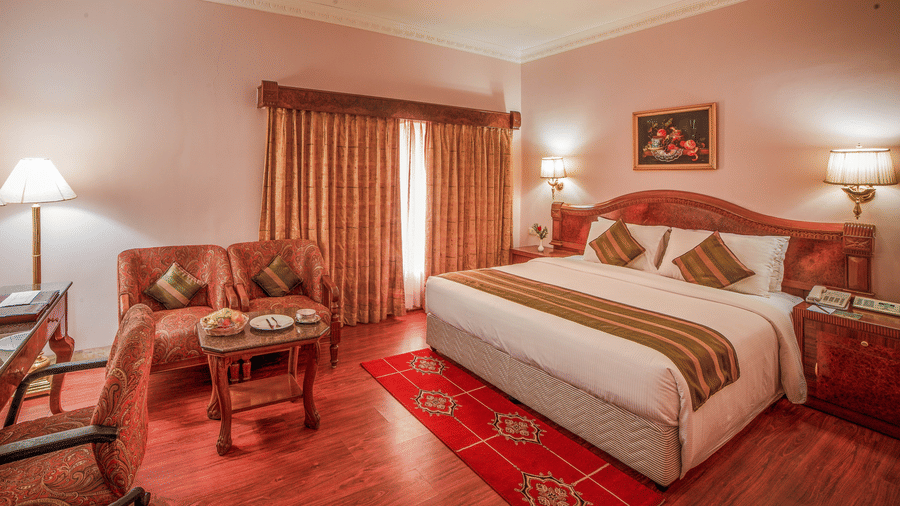 A warmly lit Superior Room offering the best accommodation in Chennai, with a king size bed, wooden decor, and cosy seating area by the window at Raj Park Hotel - Chennai