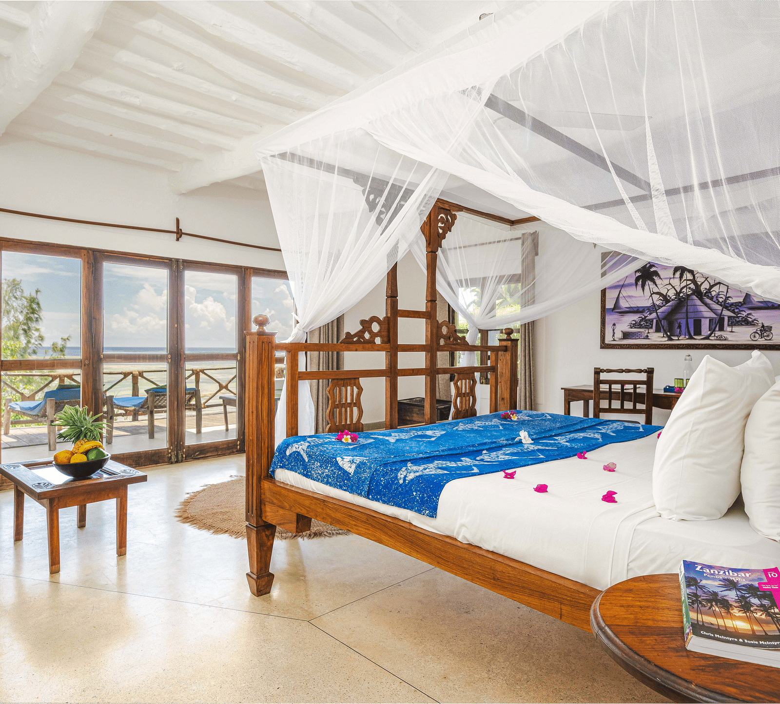 View of a room showcasing a large bed with mosquito nets and decorative pillows, a small table, and artistic wall hangings in Sea View Family Cottages - Shooting Star Boutique Hotel.