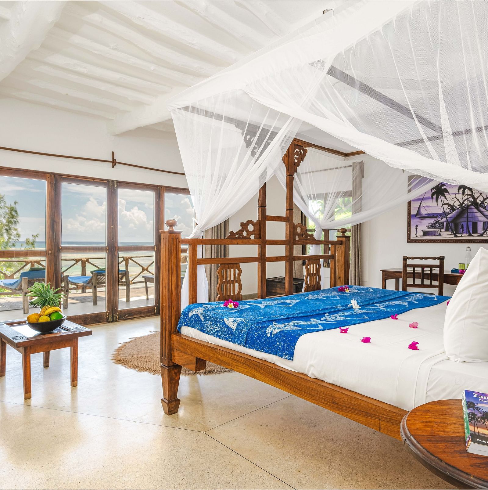 View of a room showcasing a large bed with mosquito nets and decorative pillows, a small table, and artistic wall hangings in Sea View Family Cottages - Shooting Star Boutique Hotel.