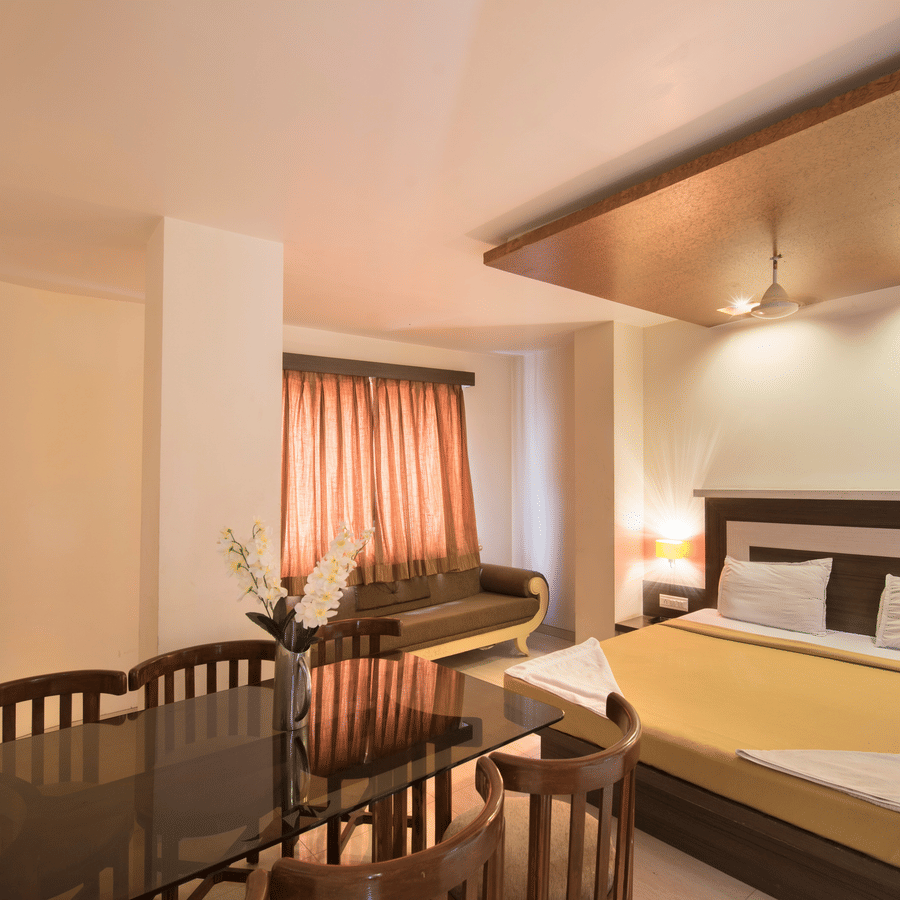 Spacious suite room containing a beige-sheeted bed, a seating sofa, and an attached dining table section.