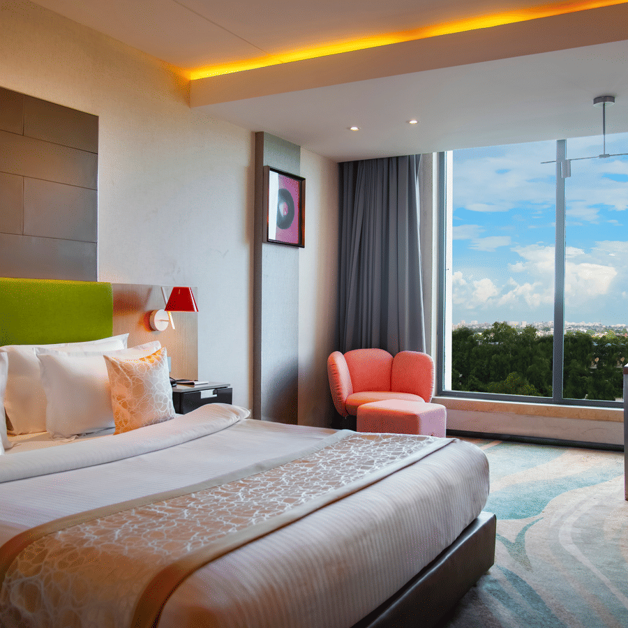 Bedroom at The Regnant featuring double size bed, a sofa,  a work desk and chair, and a large window with view.