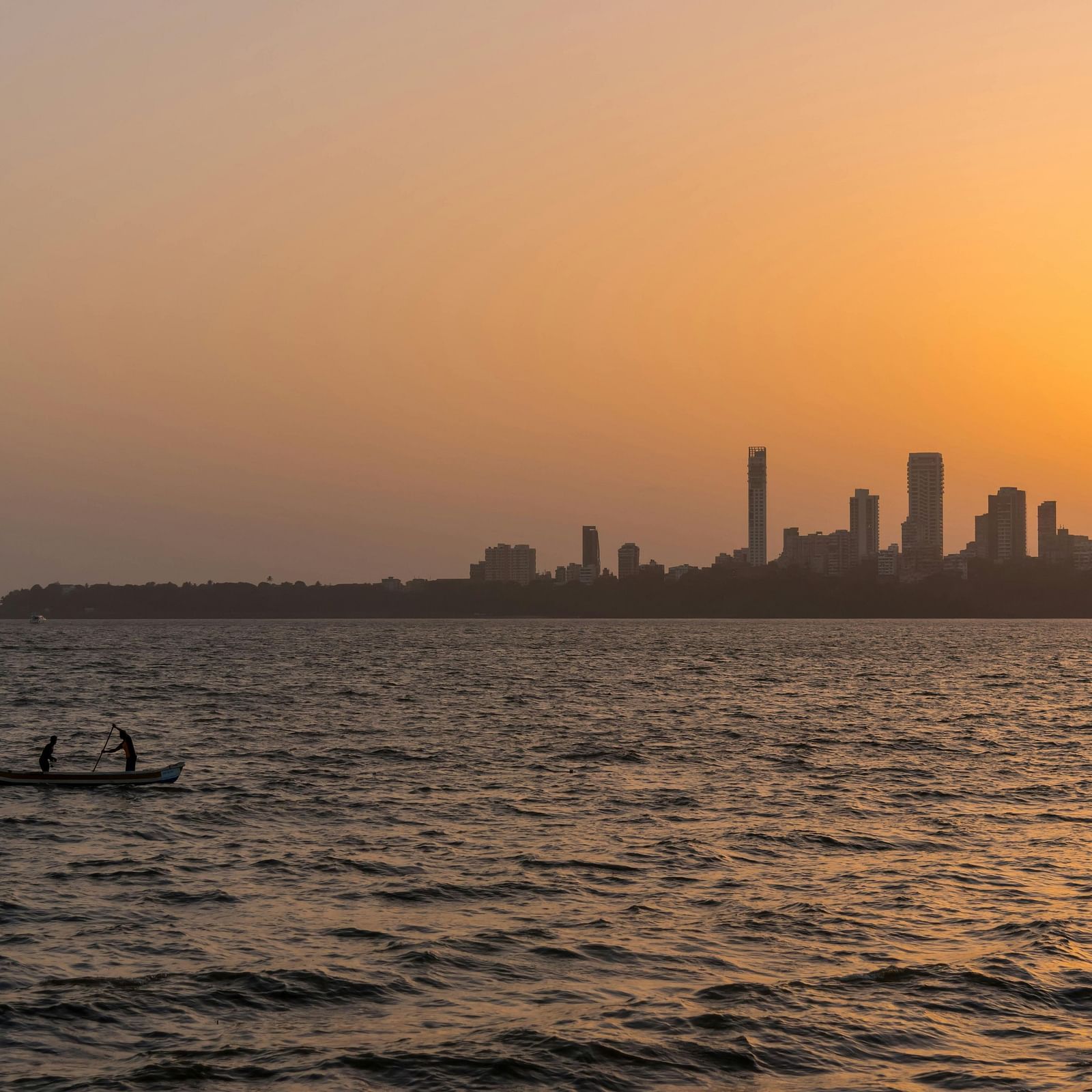 A beautiful sunset over the Mumbai skyline with a small boat in the foreground.