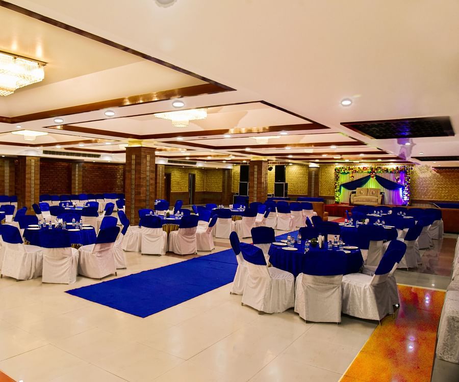 A banquet space with modern decor, bright lighting and white and blue chairs and a blue carpet laid out. - Clarks Inn Express, Near Jammu Bari Brahmana Railway Station