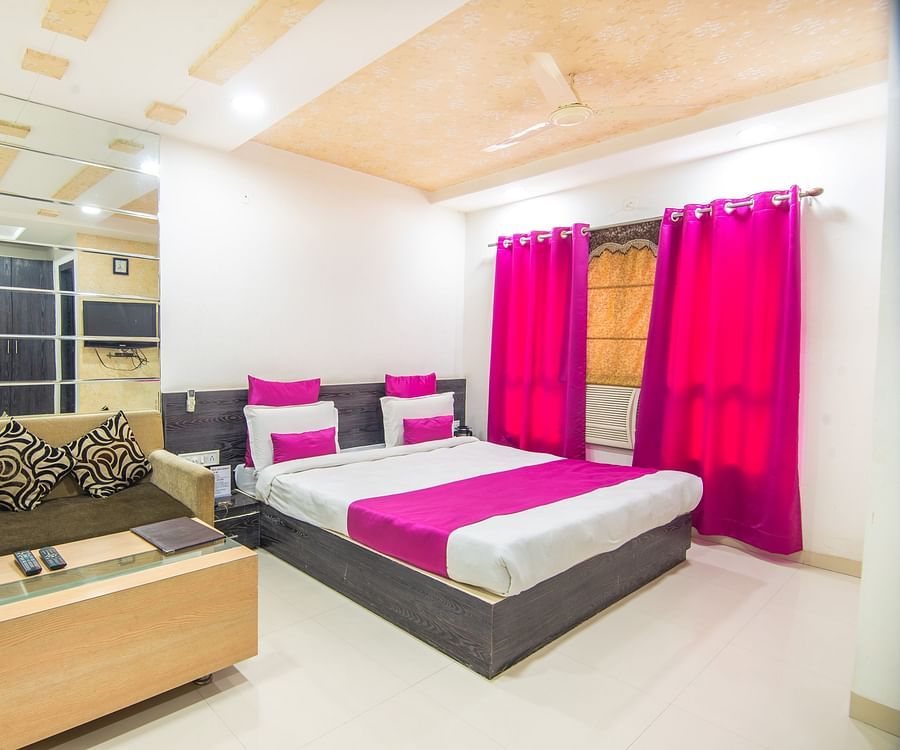 A room with a sofa bed, decorative pillows, a coffee table and violet curtains -  Hotel Morya, Bhopal