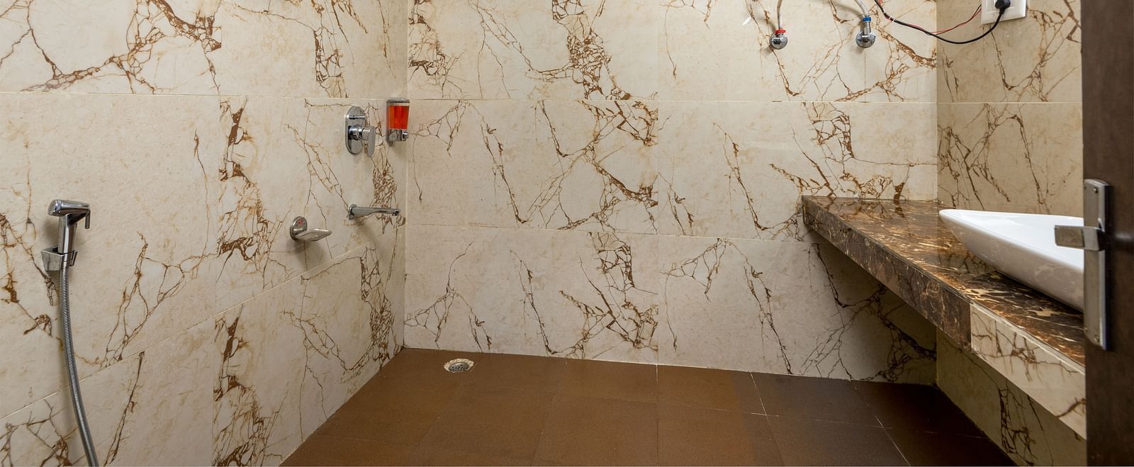 A image of the bathroom with textured tiles on the wall and a geyser and wash basin in vicinity | DLS Anupam Resort, Dharamshala