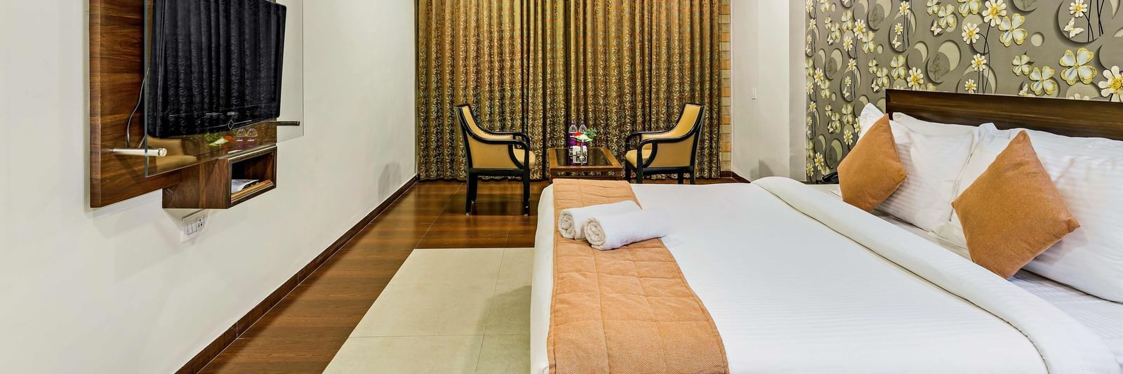 A royal executive room in Krushnai Resort featuring a double bed with yellow runners and a wall mounted TV.