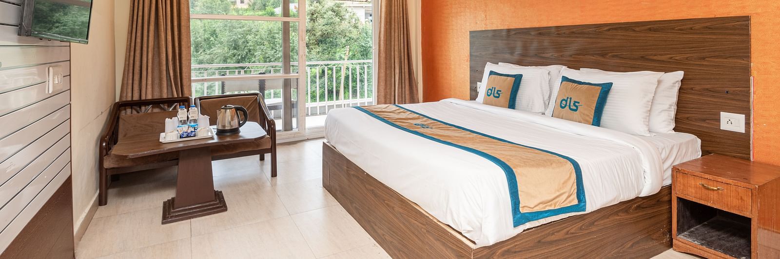 Image of a king size bed in a room with orange coloured wall and couch placed in one corner with a balcony | DLS Anupam Resort, Dharamshala