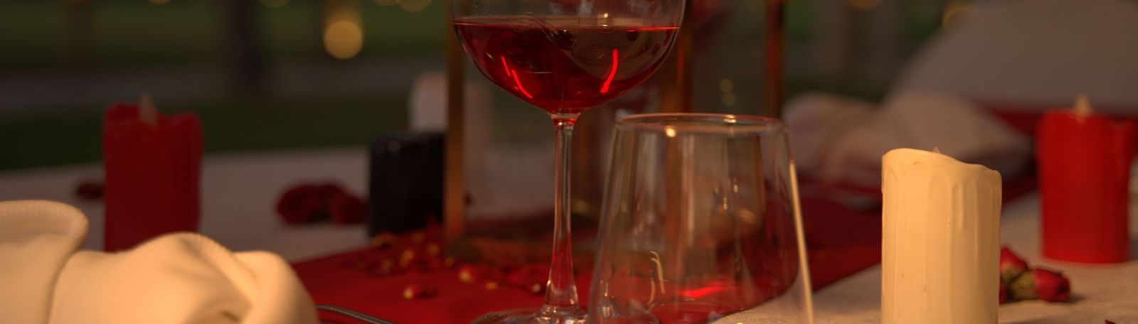 A close-up of a wine glass and candle on a red-themed dinner table - Kaldan Samudhra Palace