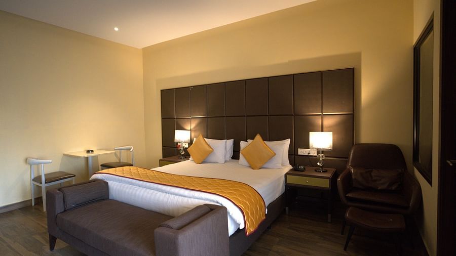 Junior Suite at Citrus Classic Resorts and Spa Mahabalipuram ECR featuring a plush bed with a divan at its foot and a couch on one side and a tiny sitting space for two on the other side of the room