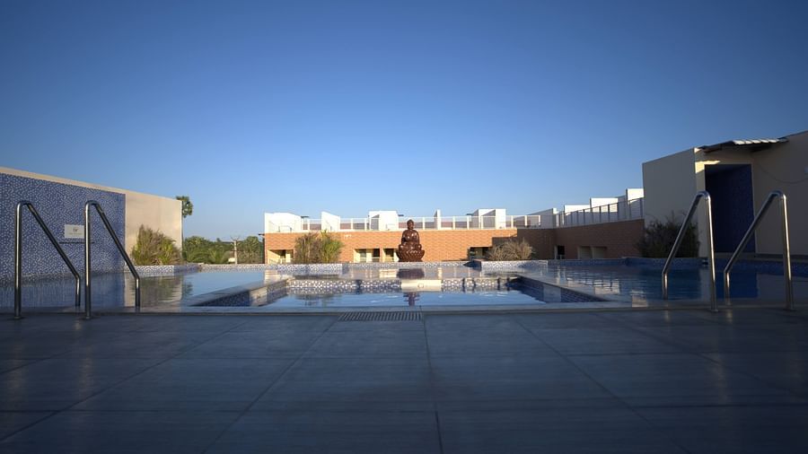 A tranquil pool with a serene Buddha statue at the center, surrounded by modern architecture and clear blue skies at Citrus Classic Resorts and Spa Mahabalipuram ECR