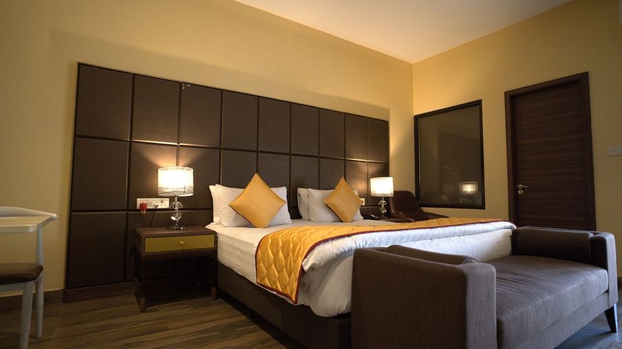 Premium Room at Citrus Classic Resorts and Spa Mahabalipuram ECR featuring a plush bed with a large headboard and lamps on both sides on the nightstand and a divan at its foot