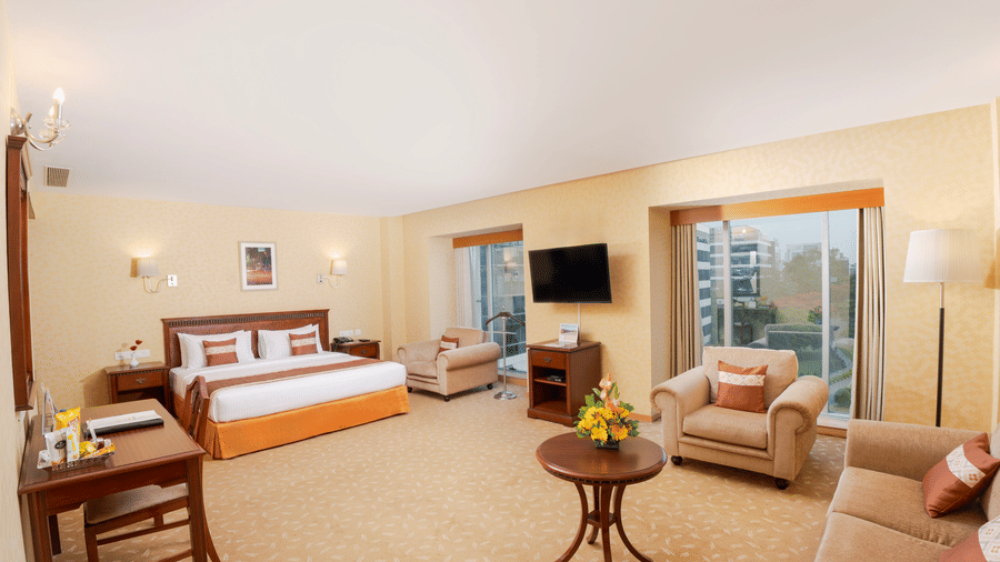 A room with a large bed, spreads, pillows, a table, a window, and a table. | MGM Mark Whitefield