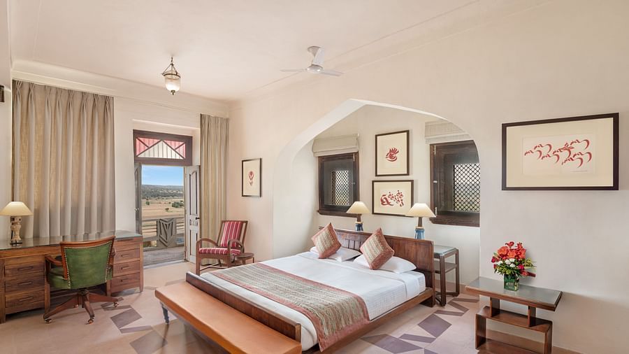Room with bed, wooden frame, patterned runner, furniture including desk, chairs, and tables, framed artwork, curtains, and patterned floor - Tijara Fort-Palace - 19th Century, Alwar.