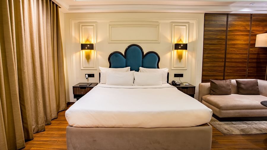 a double bed with side table and a sofa on the side inside one of the rooms - Wedlock Greens Hotel Resorts Dhanbad