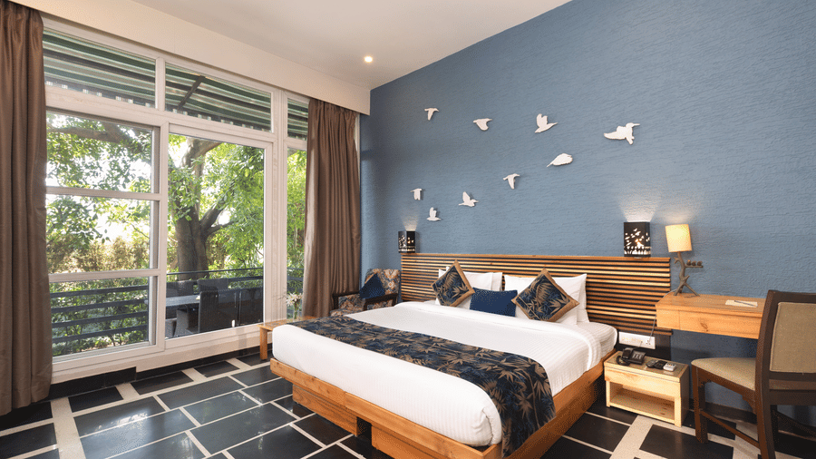 Nature View Suites view showing a bed with a dark runner and a window with curtains at The Golden Tusk, Jim Corbett