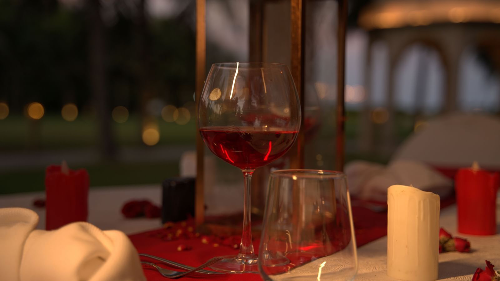 A close-up of a wine glass and candle on a red-themed dinner table - Kaldan Samudhra Palace