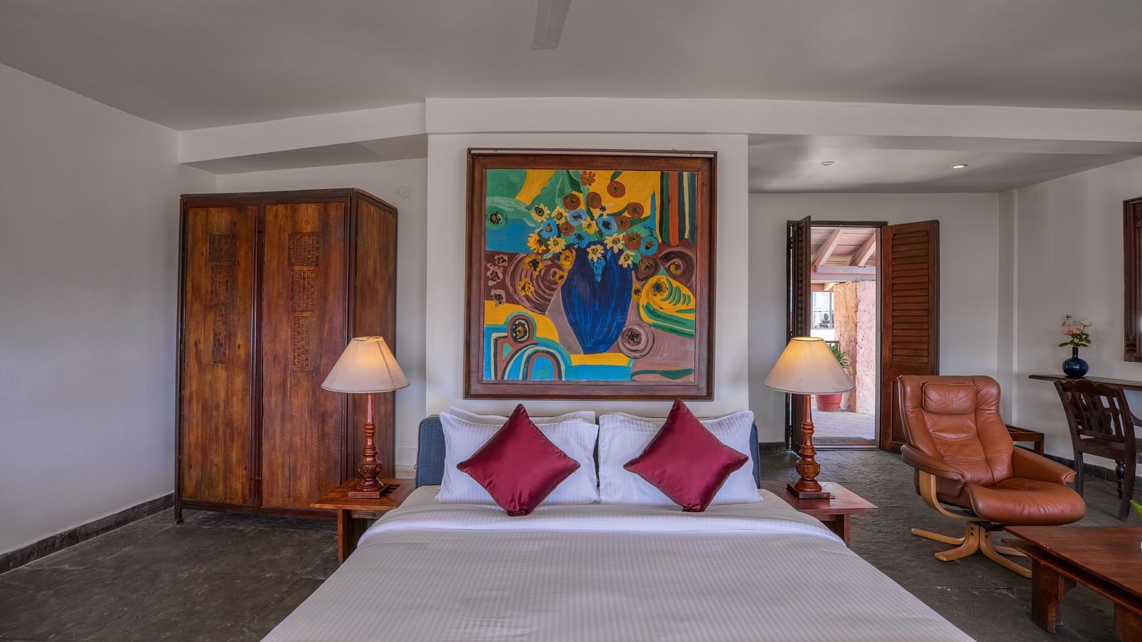 Hotel room featuring a comfortable bed with red accents, wooden furniture, and vibrant artwork. | Mango Hill, Yercaud