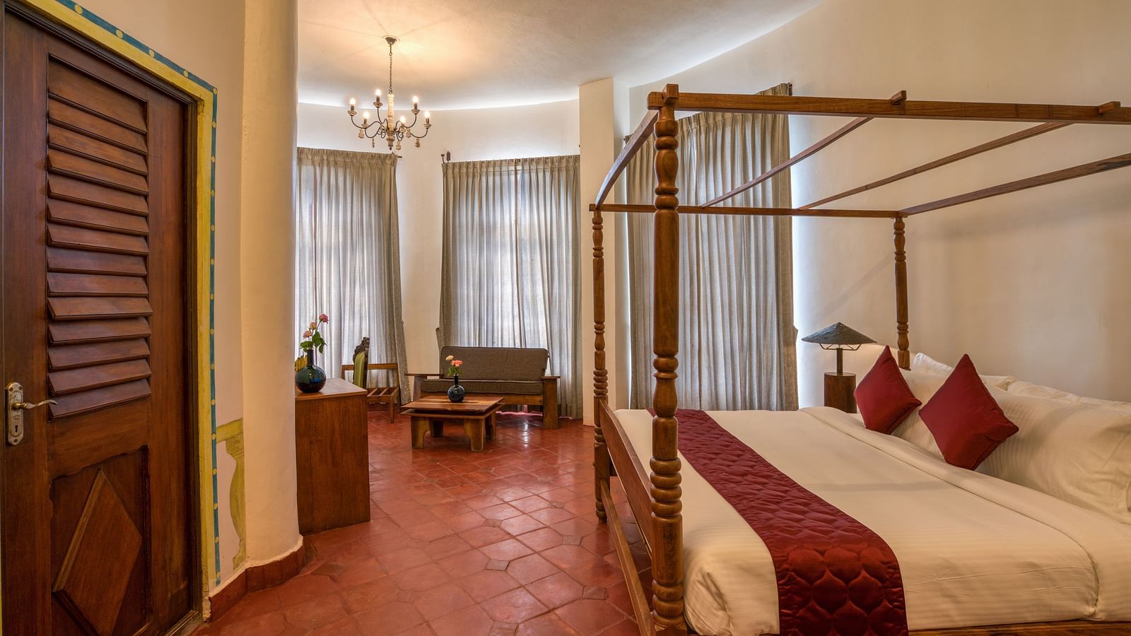 A room with four-poster bed, large windows covered by curtains and as a sitting area at one corner of the room | Mango Hill, Yercaud