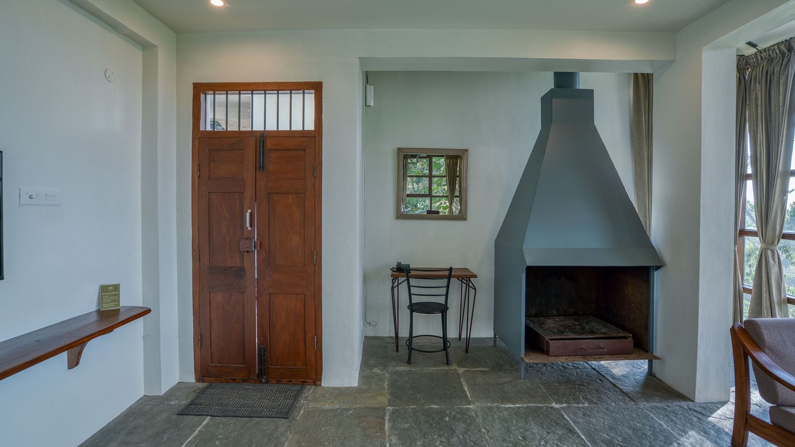 Interior of a room with a fireplace, wooden door, and a small table with a chair. | Mango Hill, Yercaud