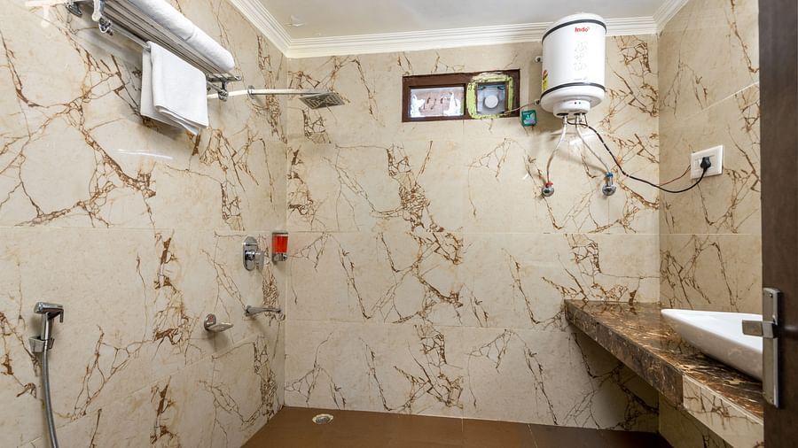 A image of the bathroom with textured tiles on the wall and a geyser and wash basin in vicinity | DLS Anupam Resort, Dharamshala