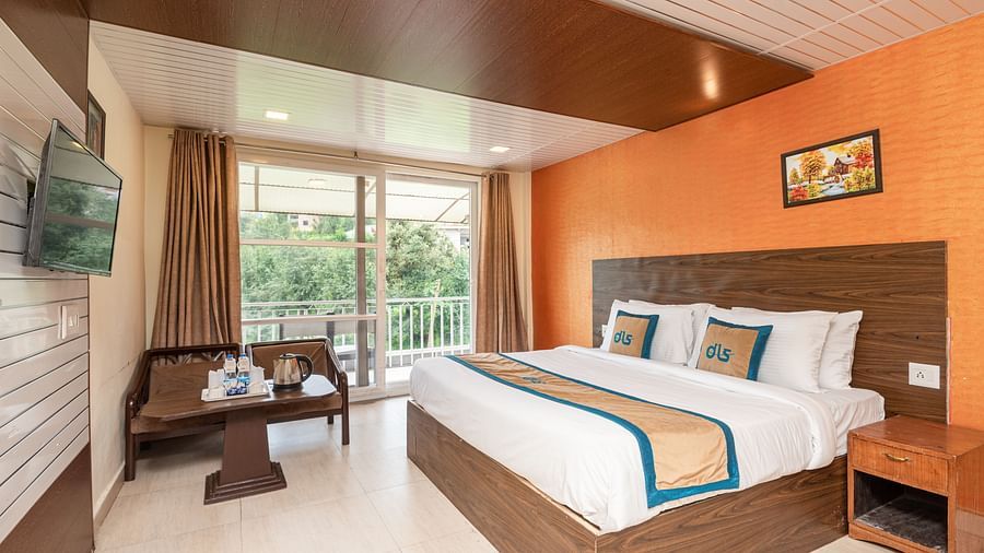 Image of a king size bed in a room with orange coloured wall and couch placed in one corner with a balcony | DLS Anupam Resort, Dharamshala