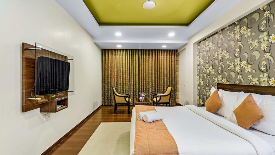 A royal executive room in Krushnai Resort featuring a double bed with yellow runners and a wall mounted TV.