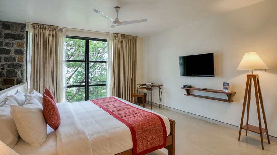A bright and airy bedroom with a large bed, a desk, and a window offering a beautiful view of the surrounding nature. | Mango Hill, Yercaud