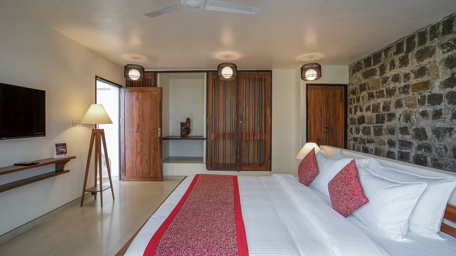 A large bedroom featuring a comfortable bed, a desk, a mounted TV, and stylish décor, with a stone feature wall and ample lighting. | Mango Hill, Yercaud