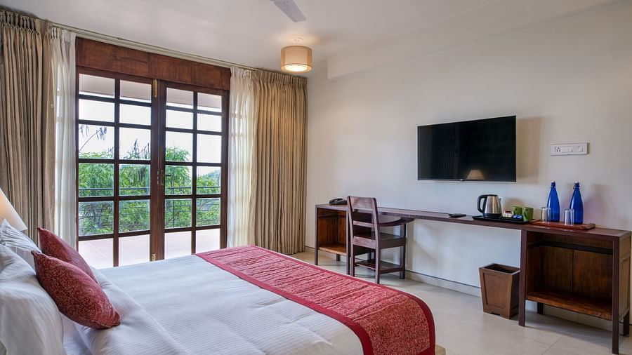 A comfortable bedroom with a desk and chair, a mounted TV, and access to a balcony with a scenic view.  | Mango Hill, Yercaud