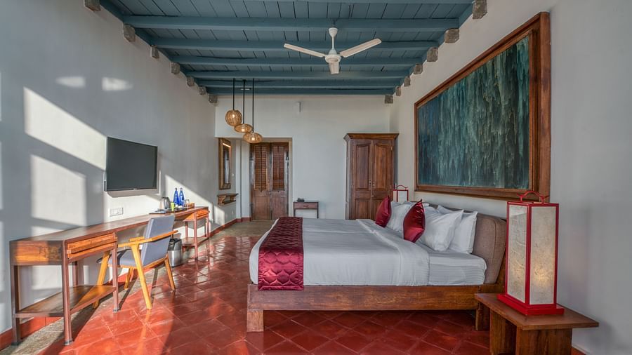 Bedroom with a king-size bed, colorful artwork, wooden furniture, and a ceiling fan, featuring a mix of modern and traditional decor. | Mango Hill, Yercaud