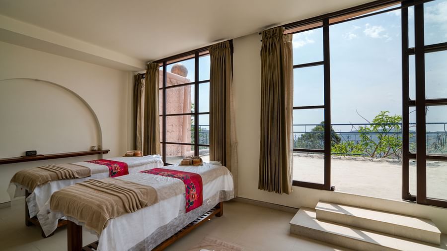 A bright spa room with two massage tables, large windows offering a scenic view.  | Mango Hill, Yercaud