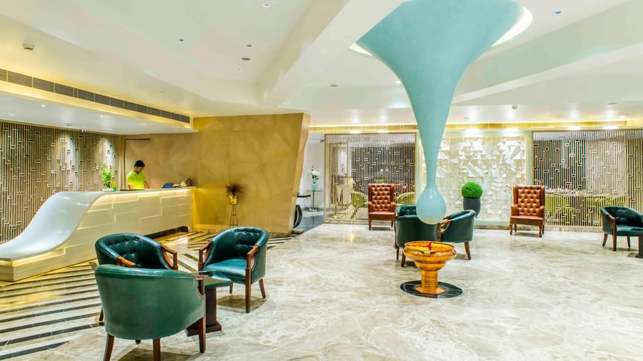 Modern hotel lobby with teal armchairs, a unique light fixture, and a welcoming reception desk | The Citi Residenci Hotel Durgapur