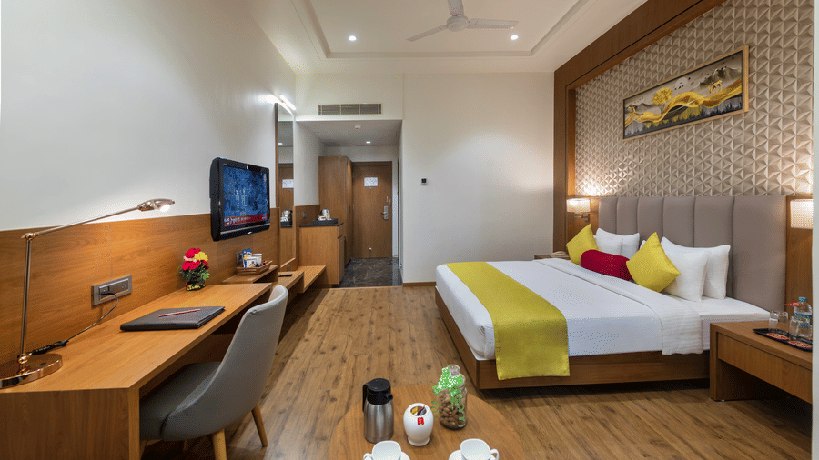 A premium room in Lords Inn Somnath with modern interiors, featuring a neatly made double bed, TV, work desk and a table set with refreshments.