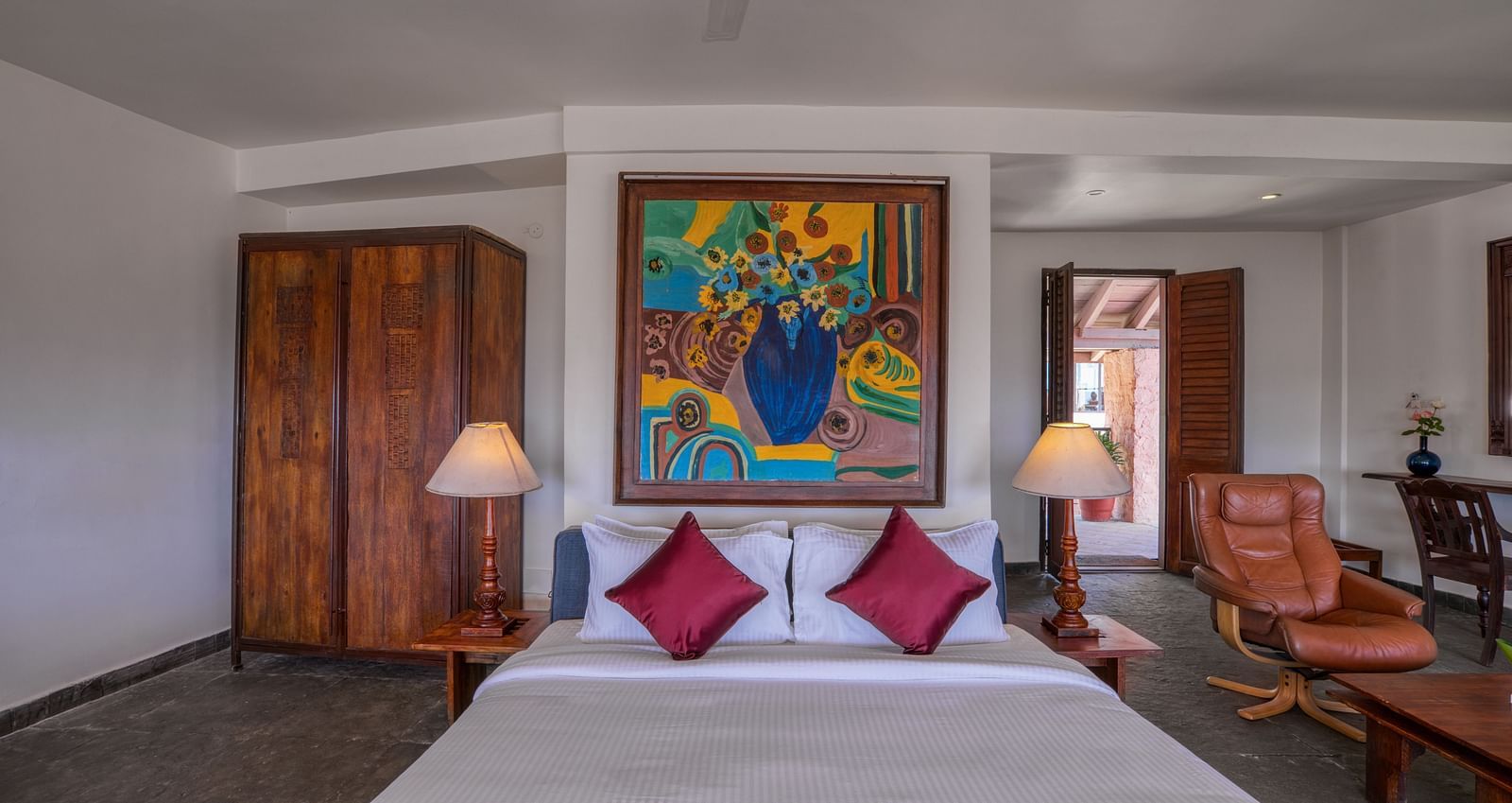 Hotel room featuring a comfortable bed with red accents, wooden furniture, and vibrant artwork. | Mango Hill, Yercaud