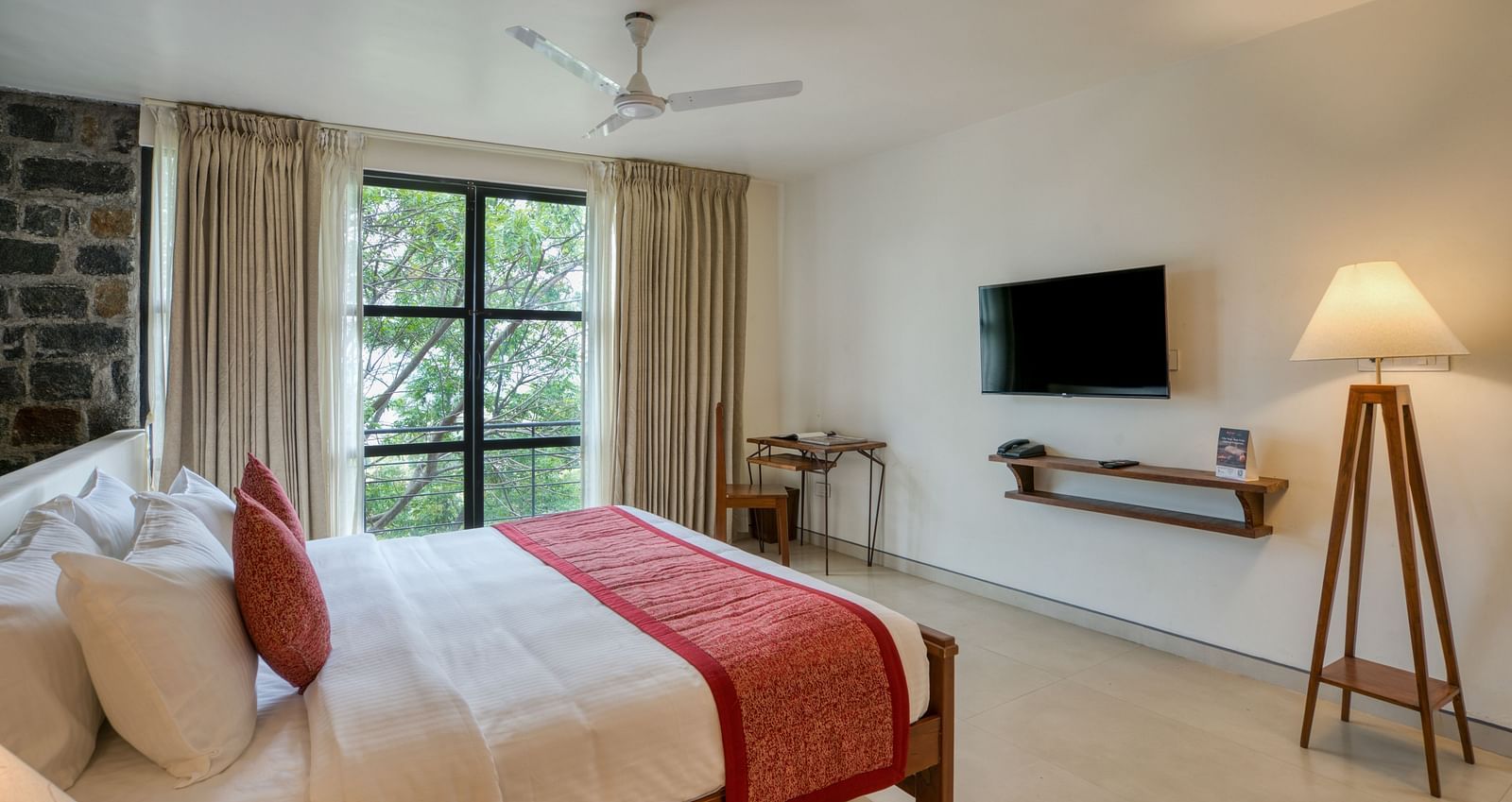 A bright and airy bedroom with a large bed, a desk, and a window offering a beautiful view of the surrounding nature. | Mango Hill, Yercaud