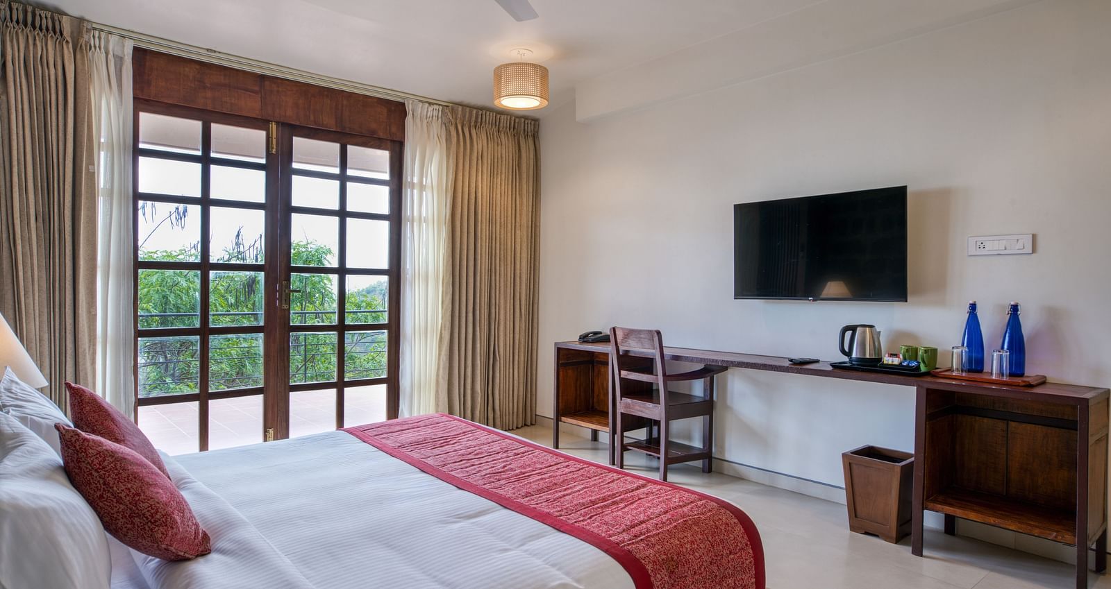 A comfortable bedroom with a desk and chair, a mounted TV, and access to a balcony with a scenic view.  | Mango Hill, Yercaud