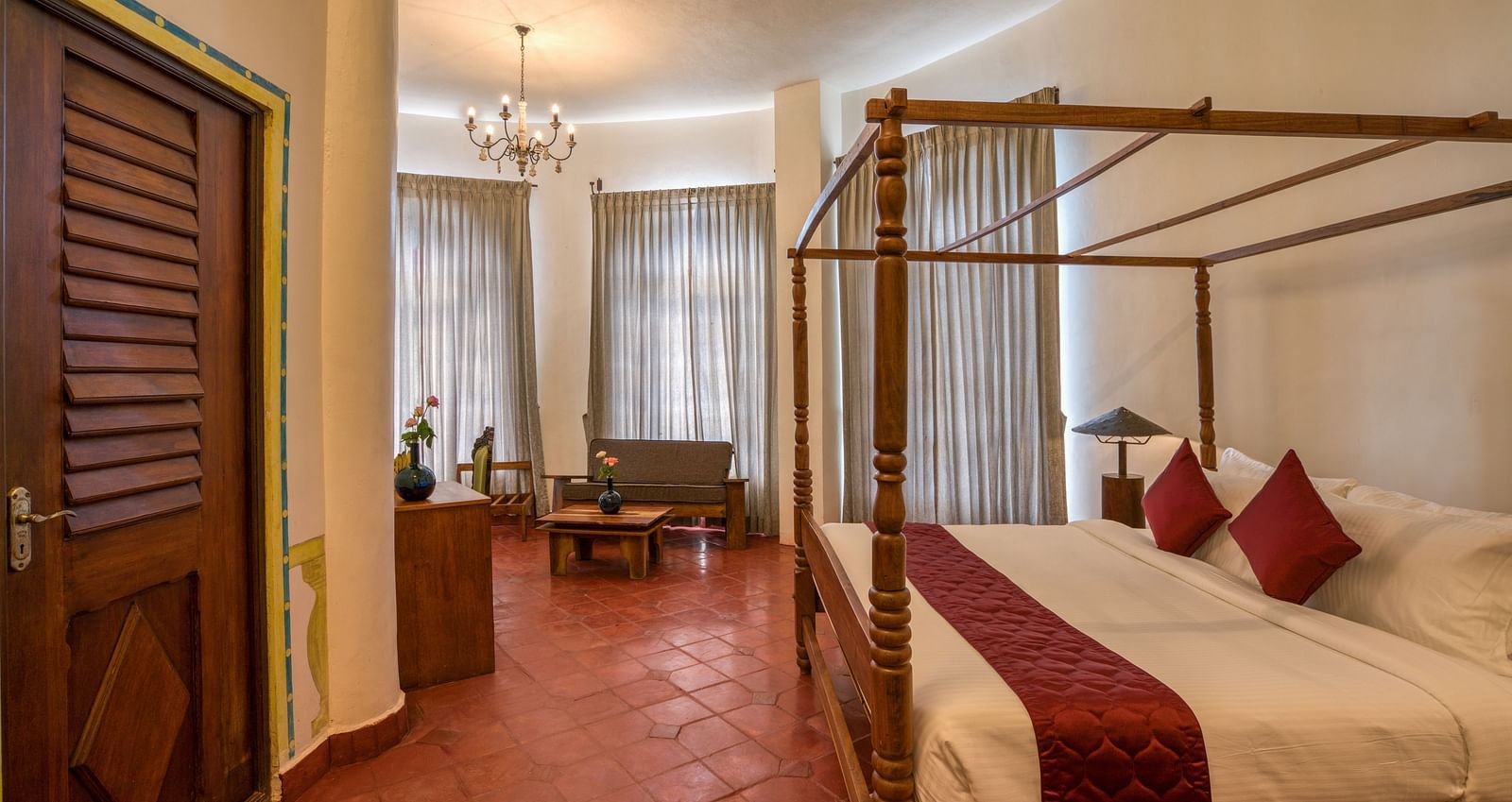 A room with four-poster bed, large windows covered by curtains and as a sitting area at one corner of the room | Mango Hill, Yercaud