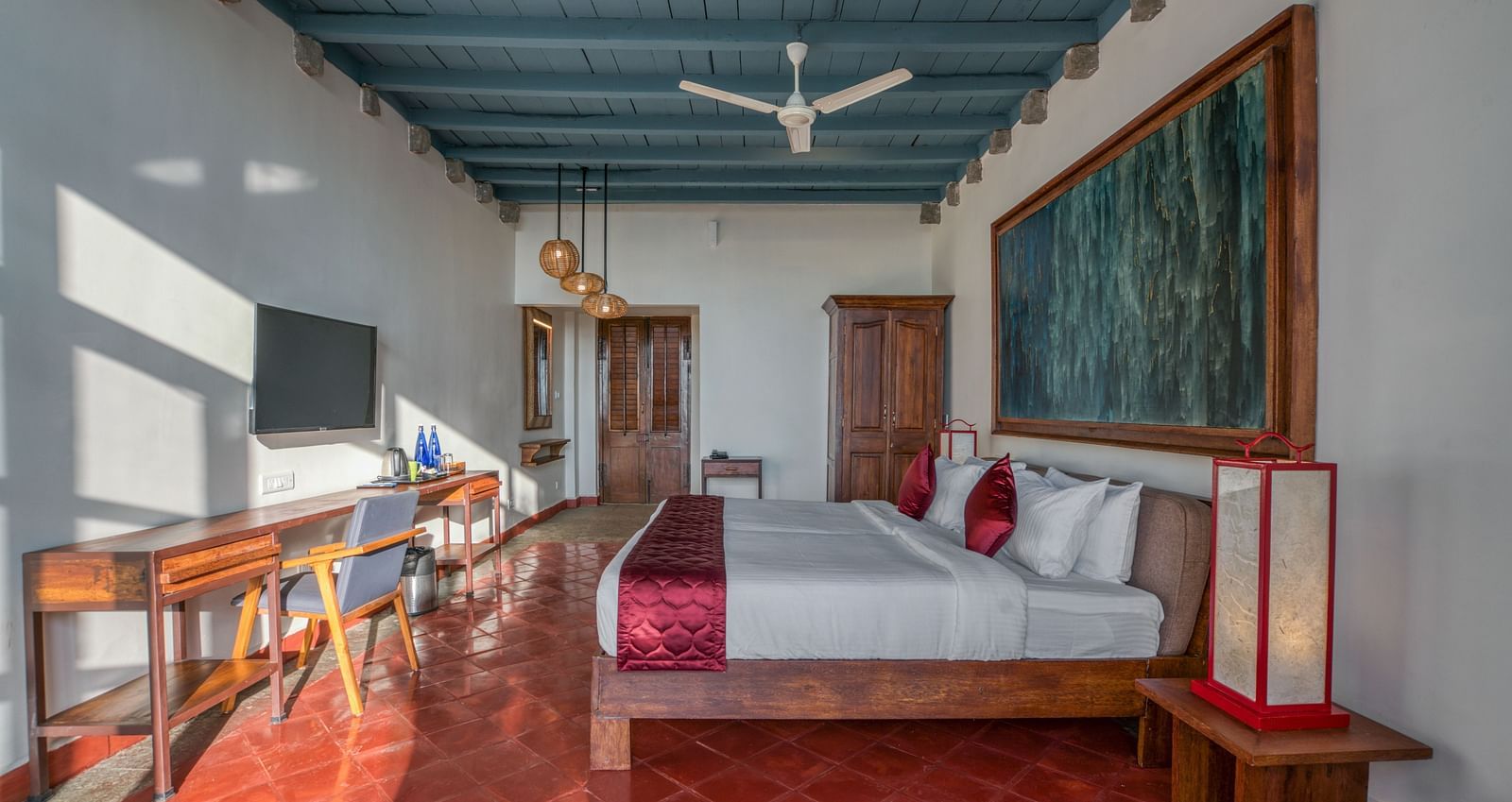 Bedroom with a king-size bed, colorful artwork, wooden furniture, and a ceiling fan, featuring a mix of modern and traditional decor. | Mango Hill, Yercaud