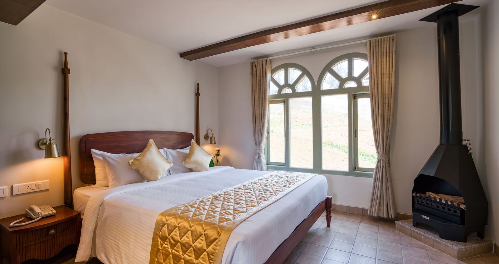 A double bed with a fireplace in the corner inside junior suite | Mango Hill Shola Ooty