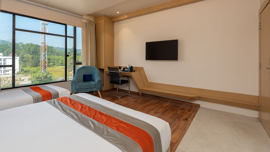 An image of a room with two beds, a work desk, two chairs and an a window overlooking the view - DLS Hotel Arihant, Haridwar