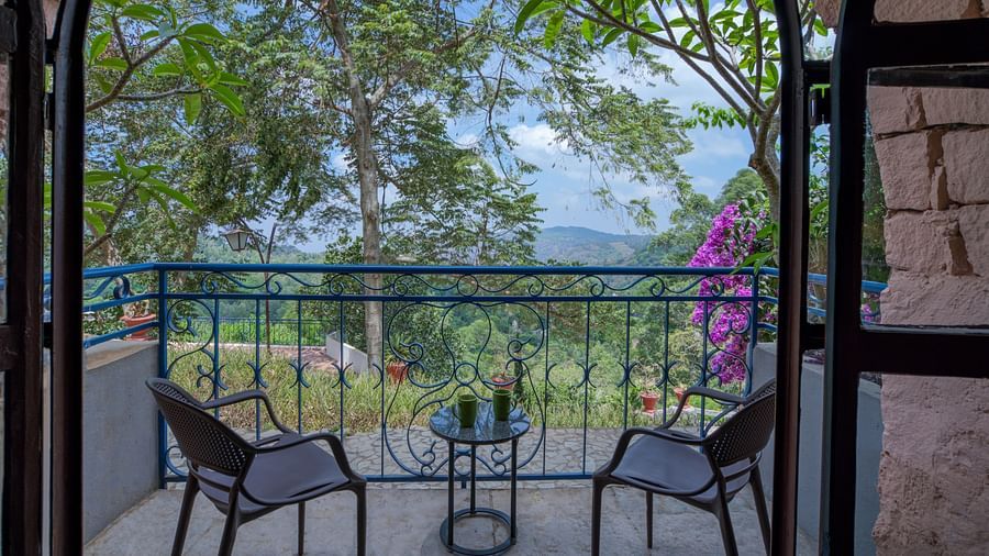 Balcony with two chairs and a table, overlooking a lush green landscape and vibrant flowers. | Mango Hill, Yercaud