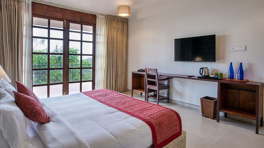 A comfortable bedroom with a desk and chair, a mounted TV, and access to a balcony with a scenic view.  | Mango Hill, Yercaud