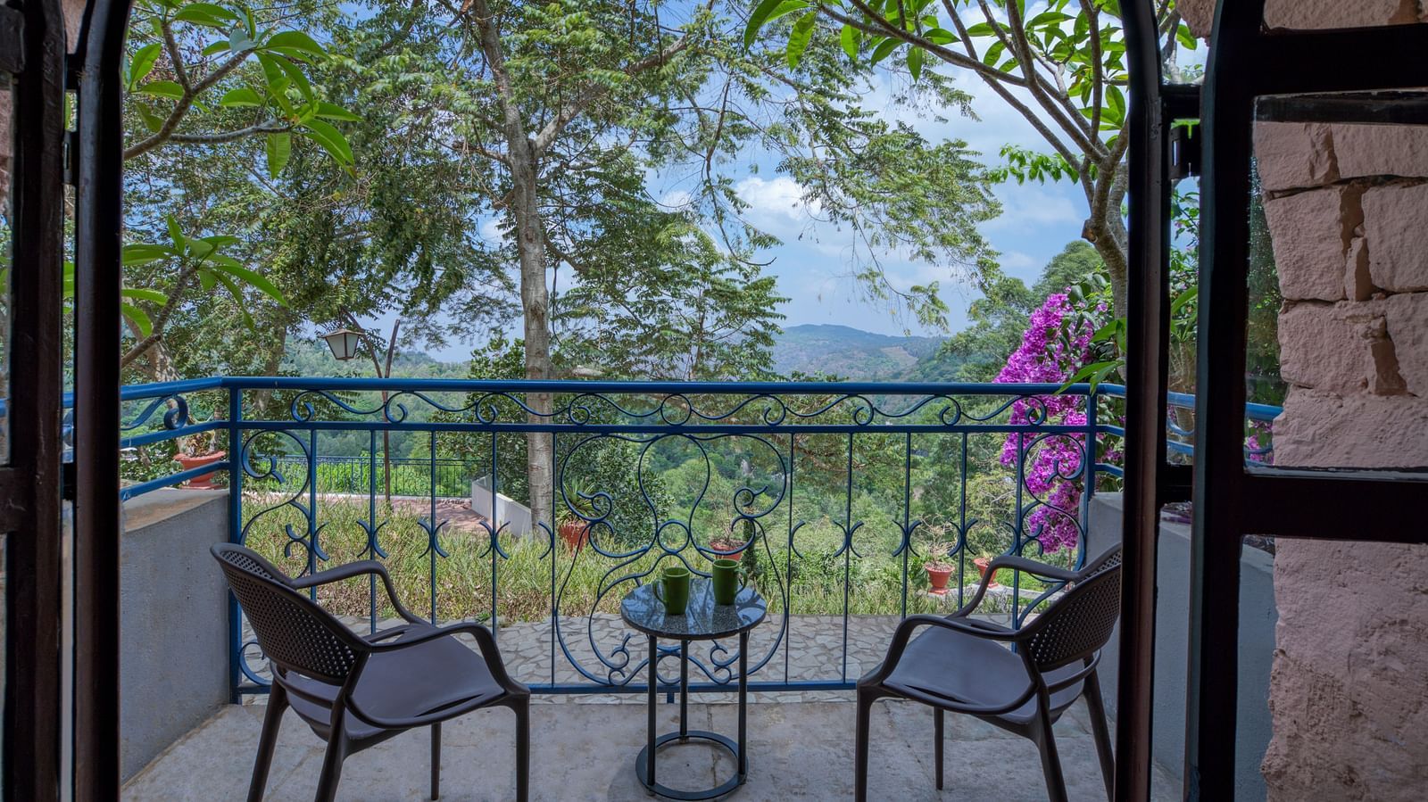 Balcony with two chairs and a table, overlooking a lush green landscape and vibrant flowers. | Mango Hill, Yercaud