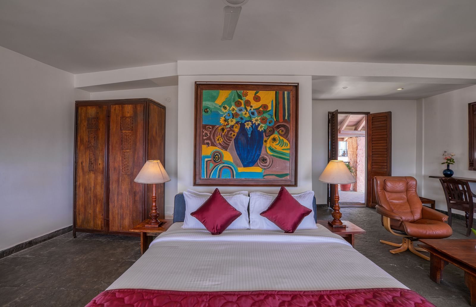 Hotel room featuring a comfortable bed with red accents, wooden furniture, and vibrant artwork. | Mango Hill, Yercaud